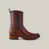 The Exotic Caiman - Brandy boot features a narrow square toe with black woven side detailing, crafted from premium brown caiman leather. It includes a wooden heel and a pull loop top, set against a light gray background.