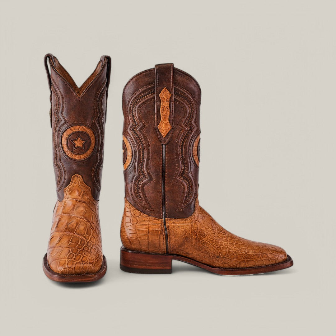 The Exotic American Alligator Hornback boots in fawn feature a square toe design, with intricately stitched, textured brown leather. They have darker brown uppers and a lighter, crocodile-like texture on the foot against a plain gray backdrop.