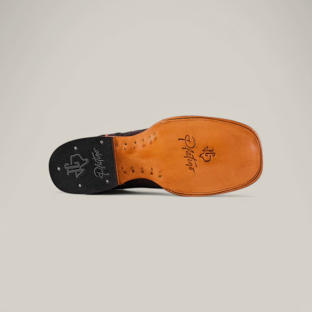 The image displays the bottom view of a handcrafted mens shoe, featuring an exotic leather sole with decorative stitching. The sole has branding and logo engravings in black and brown. A plain light background highlights the details of these Exotic Caiman Belly - Black Cherry - Square Toe boots.