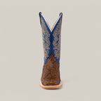 The Exotic Python - Tamarindo - Square Toe boot stands upright against a plain background, featuring a modern square toe design. The textured brown lower contrasts with the blue upper adorned with colorful zigzag stitching, and a light brown sole completes this stylish piece.