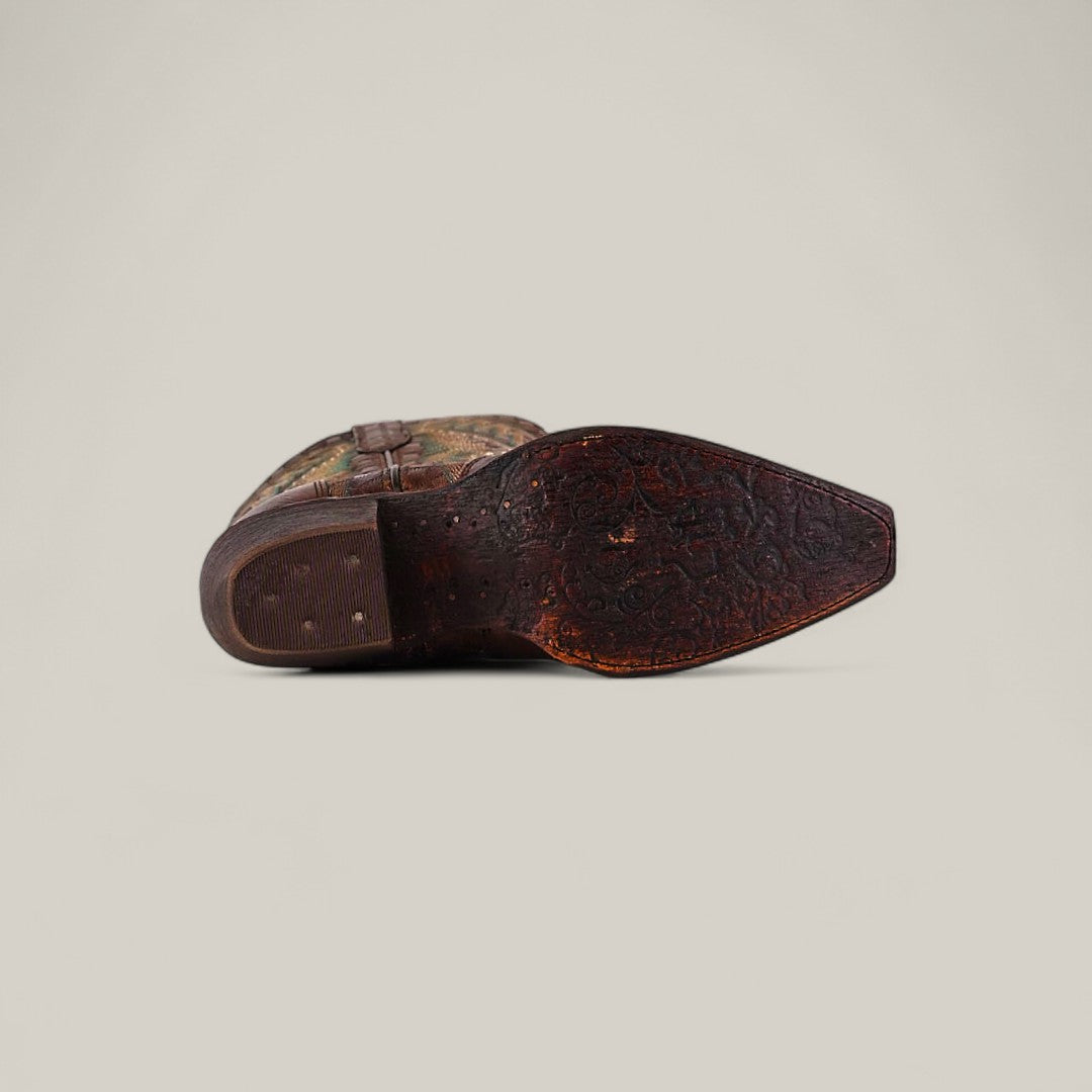 The Rachael Copper - Tall Shaft - Snip Toe boot lies on its side with the sole facing up, showing an intricate embossed pattern on the worn rich brown leather and a visible heel.