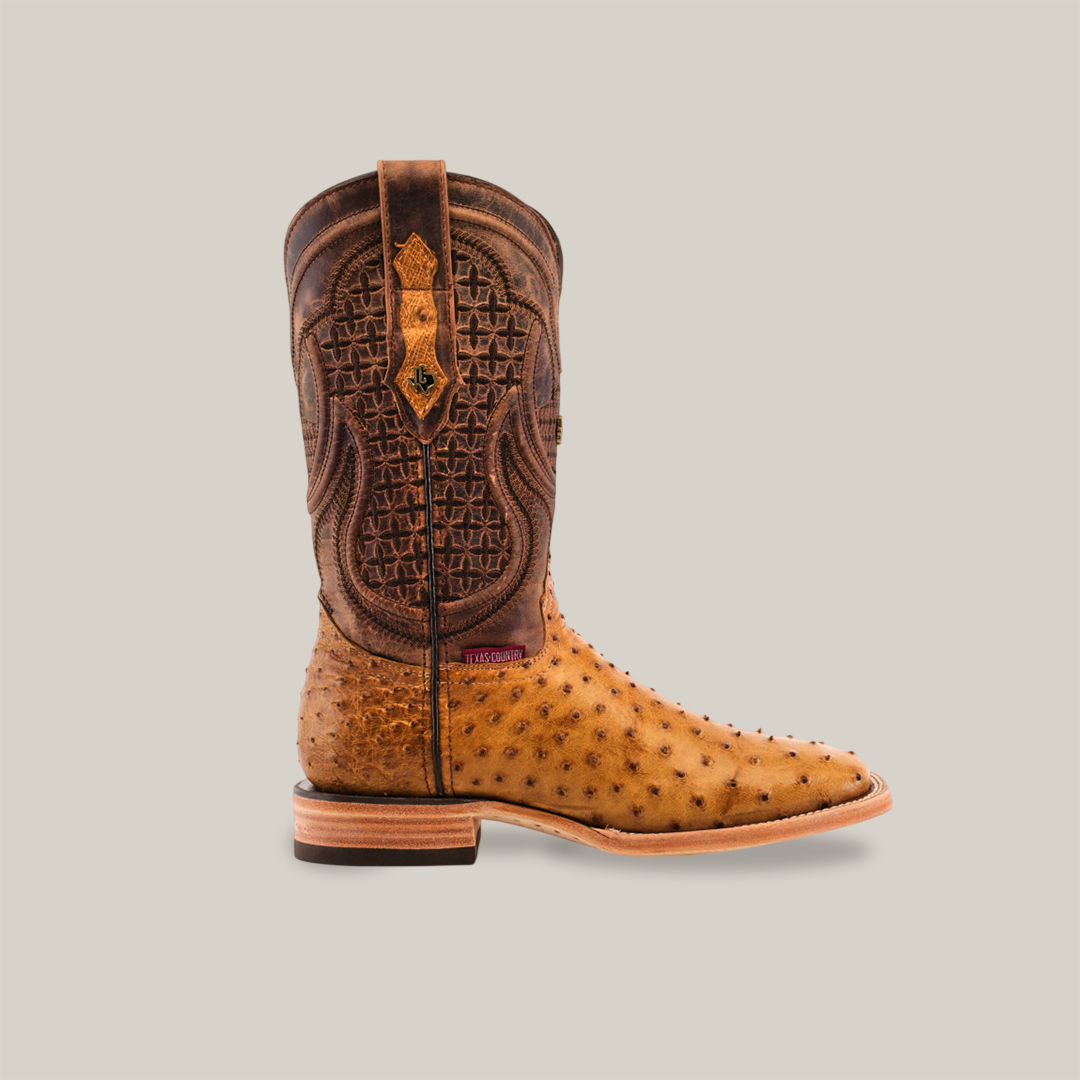 The Exotic Full Quilt Ostrich boot in fawn features a tan ostrich leather foot, a square toe, and a dark brown intricately stitched shaft with pull tabs and a wooden heel, set against a plain light background.