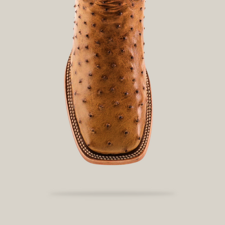 Close-up of the Exotic Full Quilt Ostrich - Fawn - Square Toe cowboy boot, showcasing its distinct bumpy ostrich leather texture and intricate stitching, strikingly set against a plain, light backdrop.