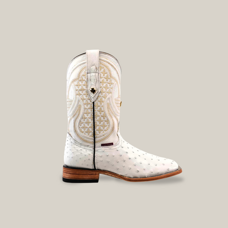 The Exotic Full Quilt Ostrich cowboy boot in white showcases intricate stitching and a unique ostrich texture on the foot. It features a square toe and wooden sole, elegantly displayed against a plain beige background.