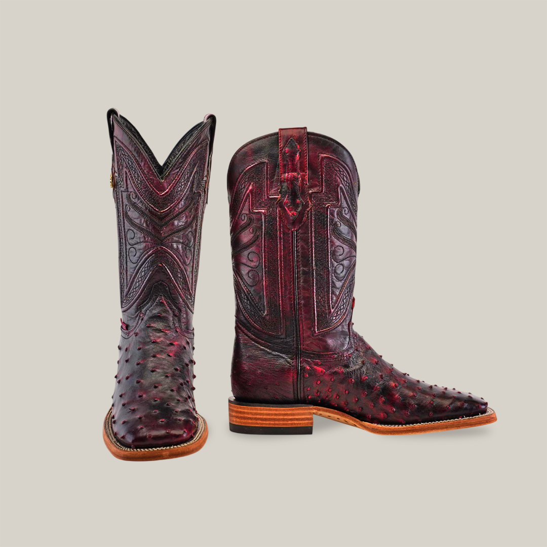 A pair of Exotic Full Quilt Ostrich cowboy boots in black cherry, crafted from genuine ostrich leather with intricate patterns and exquisite stitching, one boot upright and the other turned to display a polished wooden sole against a light background.