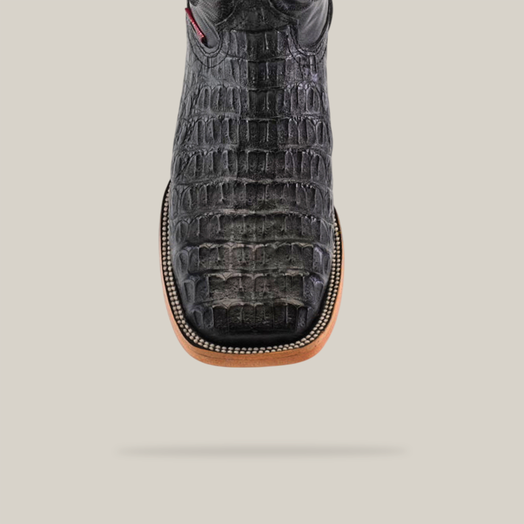 Close-up of the Exotic Caiman Horn Back boot in black with a square toe, showcasing detailed crocodile patterns and a stitched tan border against a plain light background.