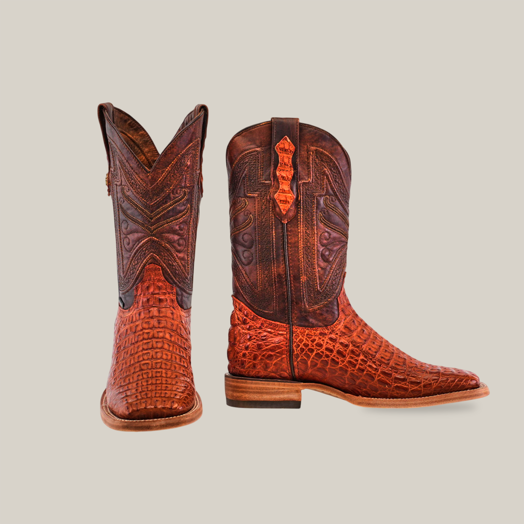 A pair of Exotic Caiman Horn Back boots in Brandy with intricate patterns. The right boot displays a square toe and detailed stitching, while the left showcases its embossed texture and low heel against a neutral background.