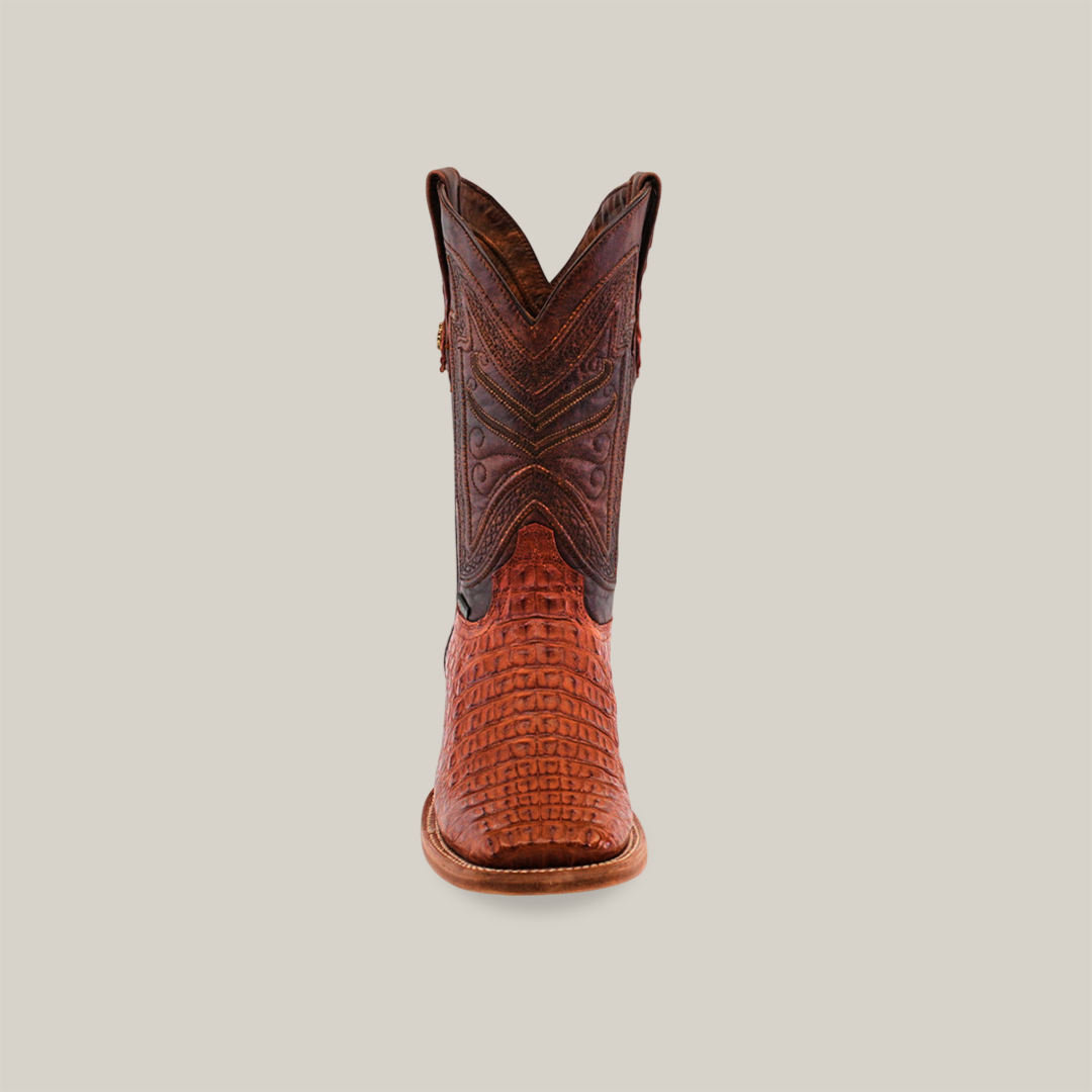 Front view of the Exotic Caiman Horn Back - Brandy - Square Toe boot, showcasing its intricate patterns and textured Caiman leather. Set against a beige background, it features detailed stitching on a darker upper section, epitomizing luxury and craftsmanship.