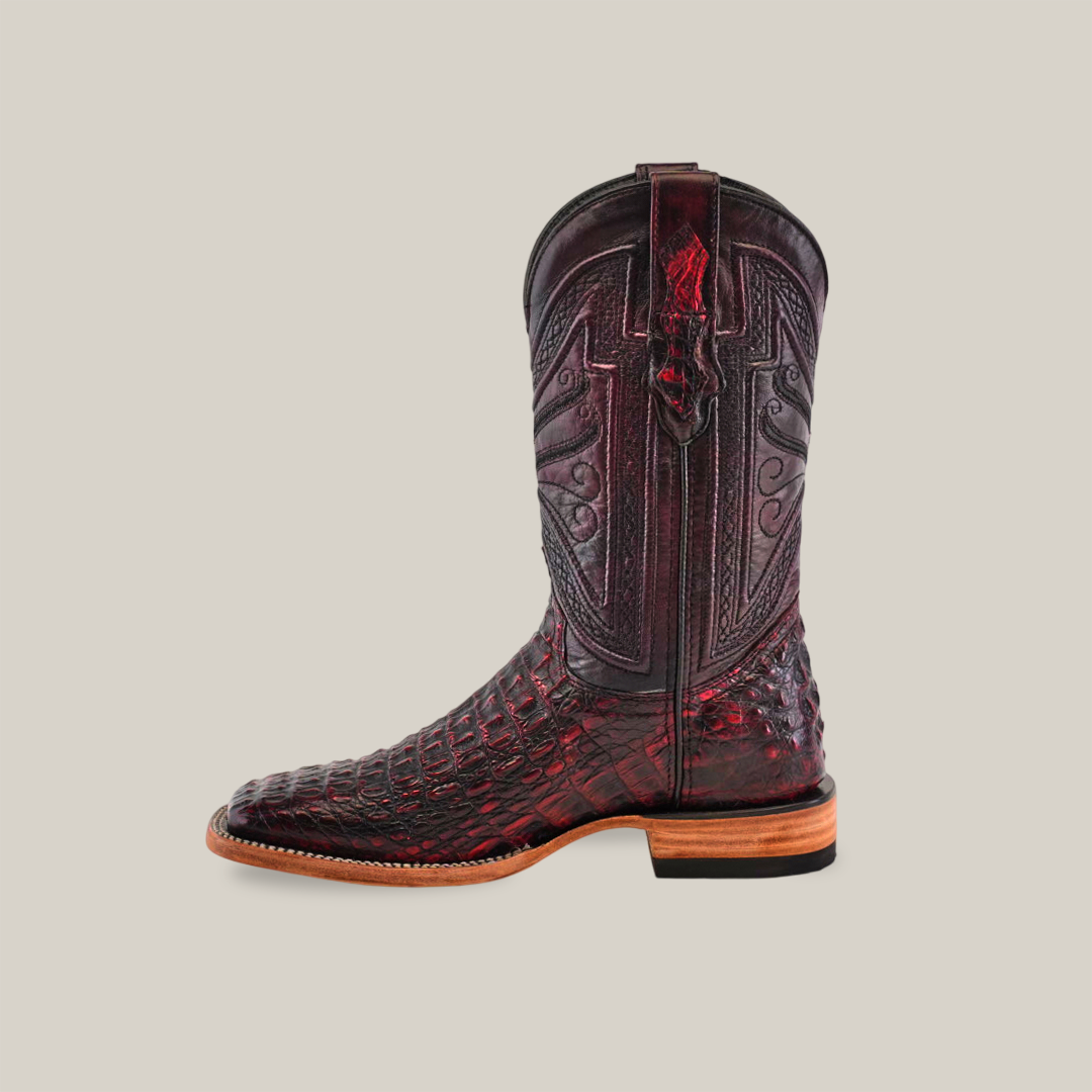 A single cowboy boot in black cherry, crafted from high-quality caiman leather with intricate texture. This exotic caiman boot has a square toe, detailed shaft stitching, and a wooden low heel against a beige background.