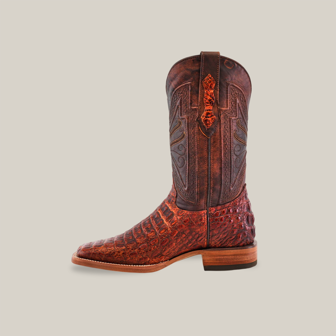 The Exotic Caiman Horn Back boot in Smoke Cogñac showcases a rustic cowboy design with textured reddish-brown leather, intricate shaft stitching, a low wooden heel, and a pointed toe against a plain beige backdrop.