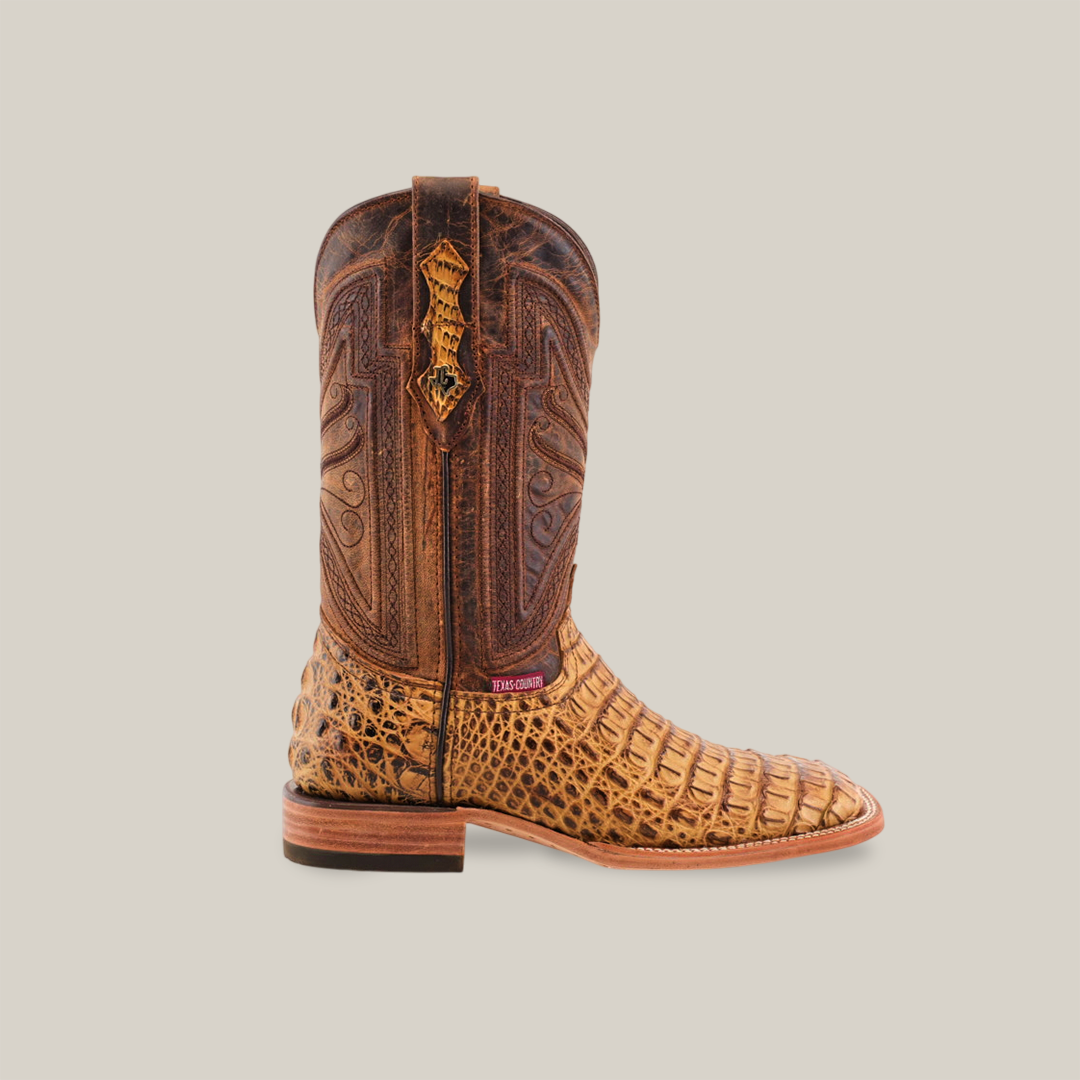 The Exotic Caiman Horn Back - Biza Camel Square Toe cowboy boot features a tan, intricately textured design with dark brown decorative stitching, a low wooden heel, and a leather pull strap. The plain background highlights its handcrafted details.