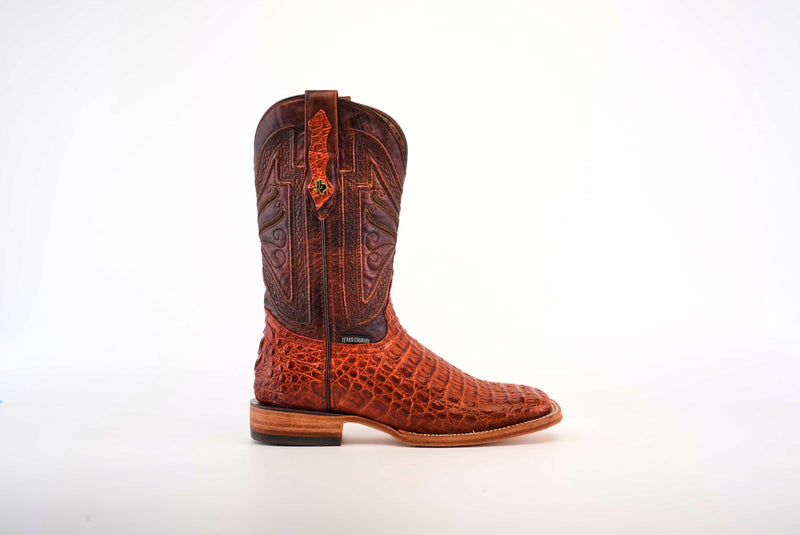 Single handcrafted cowboy boot made of exotic brown leather with an embossed pattern, decorative stitching on the shaft, and a leather pull strap, displayed against a white backgroun