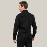 A light-haired man faces away against a gray background, wearing the Men’s Single Pocket Logo Modern Fit Stretch Dress Shirt in black (CTL9258) paired with dark pants, showcasing a contemporary silhouette.