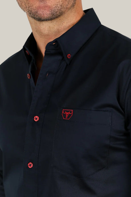 A person is wearing the Men’s Single Pocket Logo Modern Fit Stretch Dress Shirt in navy, featuring red buttons and a red logo on the chest pocket, against a light gray background.