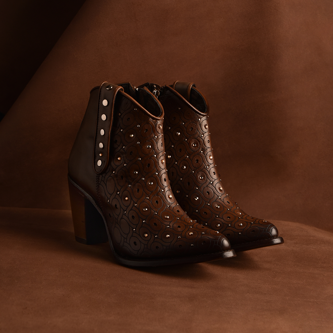 The Maple Laser & Crystals & Studs - Round Toe ankle boots feature brown leather with laser details, metal studs, a chunky heel, and side zippers, all set against a matching brown background to blend style and craftsmanship.