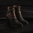 The Black Stingray Laser & Woven - Round Toe womens boots, featuring intricate embossed patterns and elegant rich brown leather accents, are displayed on a dark reflective surface. The woven round toe design beautifully complements the detailed floral interior lining.