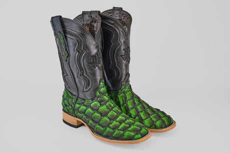 The Conor - Swamp Green - Square Toe boots feature black leather uppers, bright green scale-patterned lowers inspired by Pirarucu fish, and light tan soles and heels, shown on a light gray background.