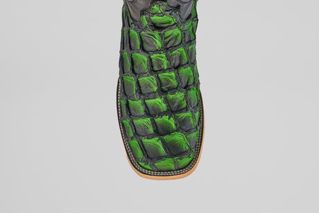 A close-up, top view of the Conor - Swamp Green - Square Toe boot showcases green and black scale-textured leather with visible stitching on a tan sole, all set against a plain white background.