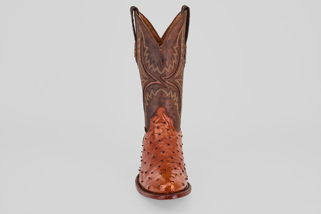 A single Exotic Full Quilt Ostrich - Brandy - Round Toe cowboy boot in brown, handcrafted with decorative stitching and a shiny quilted ostrich leather finish, shown from the front against a plain light background.