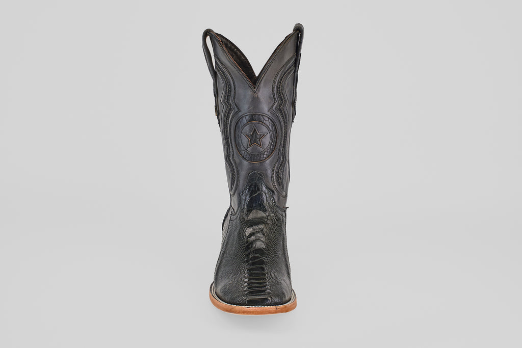 The Austin Leg - Black - Square Toe boot features decorative stitching, a star emblem on the shaft, and a light tan sole. Photographed from the front on a plain light gray background, it's ideal for square toe boot enthusiasts.