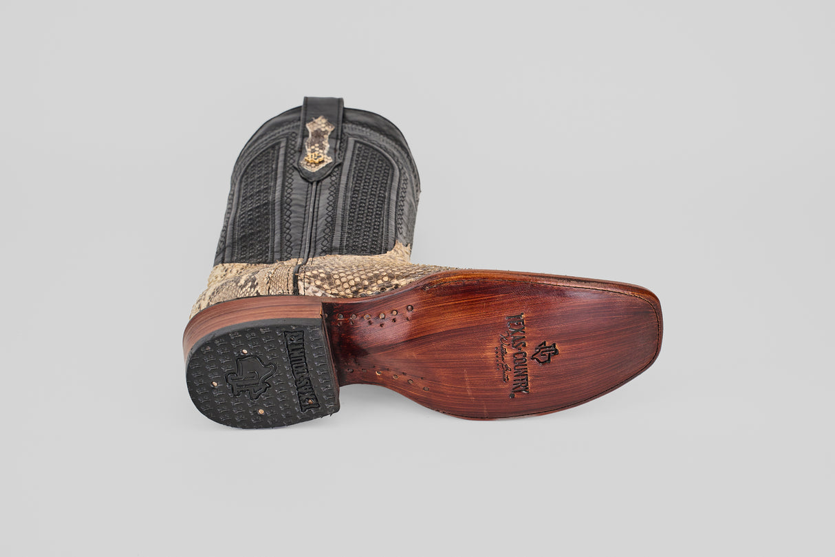 The Tanner - Natural - Narrow Square Toe boot features a black upper, tan python leather foot, and a carved wooden sole with embossed branding and star details, shown against a light gray background.