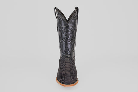 The Tanner – Matte Black – Roper Toe boot stands upright on a light brown sole, featuring a scaly texture and stitched star emblem on the shaft, showcasing western style against a clean white background.