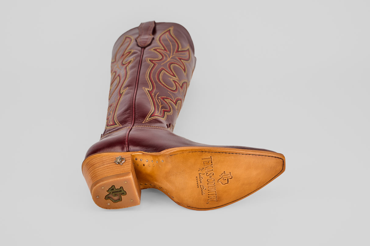 A single Allison Blackberry Tall Shaft Snip Toe boot lies on its side, showcasing decorative stitching and a green logo on the heel—classic Western boots for women. The tan leather sole is stamped with the “TX Country” logo.