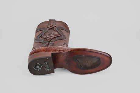 The James Platinum - Dark Cogñac - Roper Toe (Diamond) men’s western boot is shown from the bottom, featuring a brown leather upper, textured sole with branded logo and signature, stitched detailing on heel, and a plain light background.