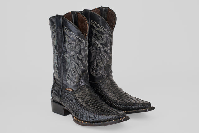 A pair of Python Black - Embossed Leather - Versy Toe (E202) cowboy boots with intricate silver stitching, pointed toes, and stacked heels is displayed on a plain light gray background.