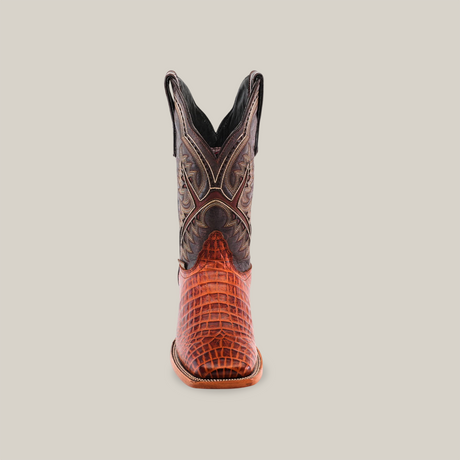 The Caiman Belly Print Cogñac - Square Toe features a single cowboy boot with an intricate reddish-brown Caiman Belly Print lower and a dark brown upper adorned with decorative stitching, elegantly standing against a plain white background.