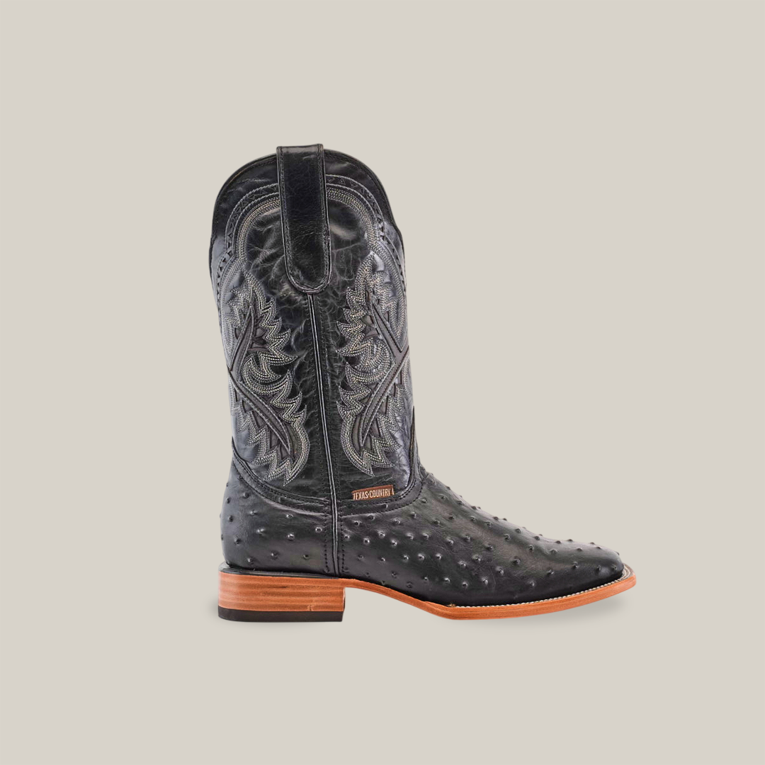 Discover the Karoo Ostrich Print Black boots, crafted from premium cowhide leather. These black cowboy boots feature intricate shaft stitching, a square toe, and a low wooden heel. The textured surface stands out beautifully against the plain white background.