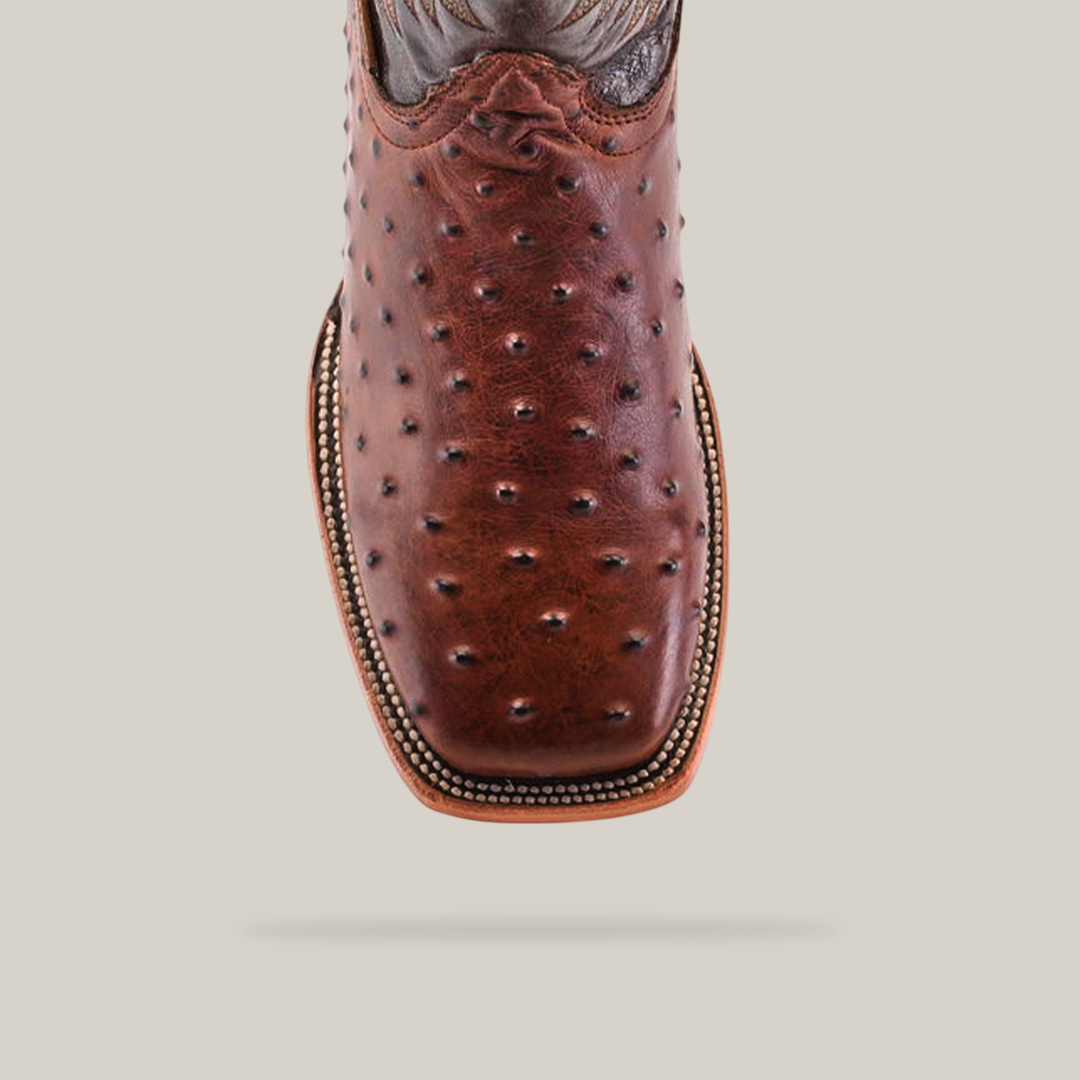 A close-up of the Karoo Ostrich Print Chocolate - Square Toe boot highlights its textured brown leather with a stitched edge design. This handmade masterpiece showcases a square toe, a detailed upper section, and a polished finish.