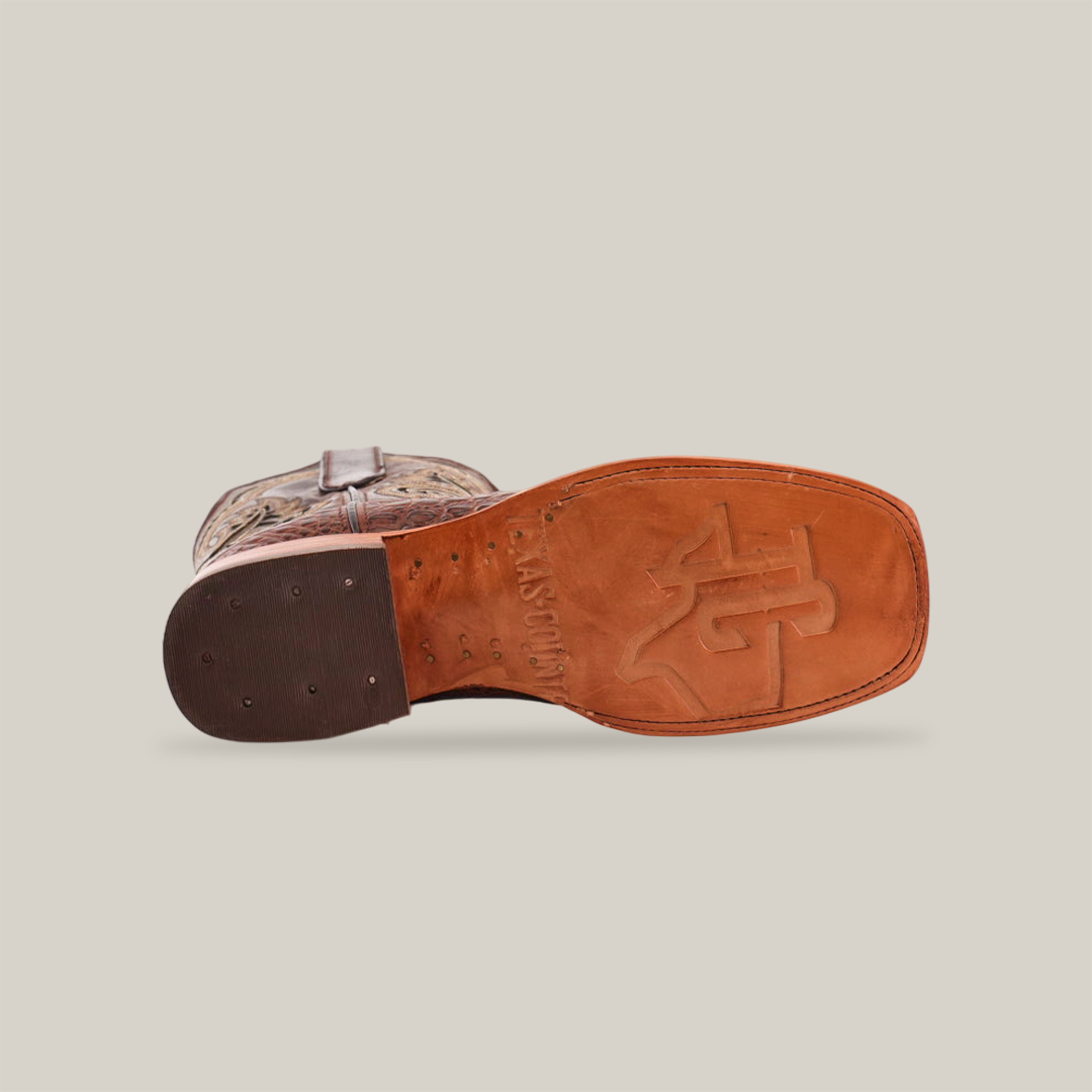 The image displays the sole view of a handmade Caiman Belly Print Chocolate square toe cowboy boot, featuring a brown sole with an embossed logo, a wooden heel with metal studs, and a patterned upper visible at the edge.