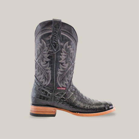 The Caiman Belly Print Black - Square Toe boot is crafted from premium cowhide leather, featuring intricate floral stitching and a distinctive Caiman belly print on the lower half. It has a wooden heel and sole, with a label on the side, presented against a plain white background.