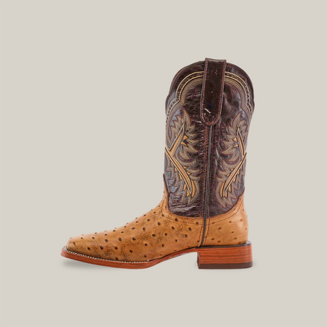 A single cowboy boot with a light brown Karoo Ostrich Print Orix leather foot and dark brown shaft, features intricate stitching. It stands against a white backdrop, showcasing its square toe and wooden heel.