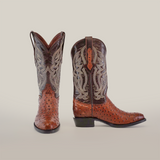 The Karoo Ostrich Print Chocolate - Round Toe luxury cowboy boots, crafted from cowhide leather, are displayed on a plain white background. These brown boots feature intricate gray stitched patterns on the shaft, with the left boot facing forward and the right boot shown from the side.