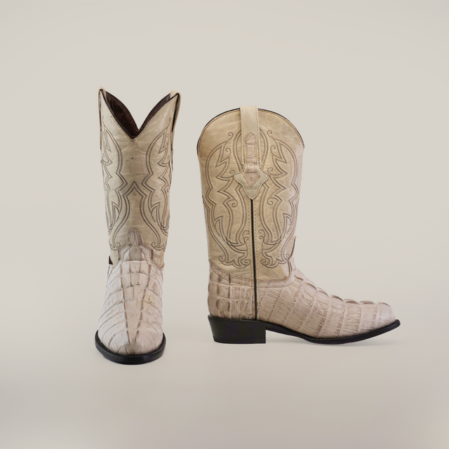 A pair of handmade cowboy boots, crafted from premium cowhide, features intricate stitching with a crocodile tail print texture. Named Crocodile Tail Print Bone - Round Toe, these white boots have a pointed toe design and display one boot facing forward and the other stylishly to the side.