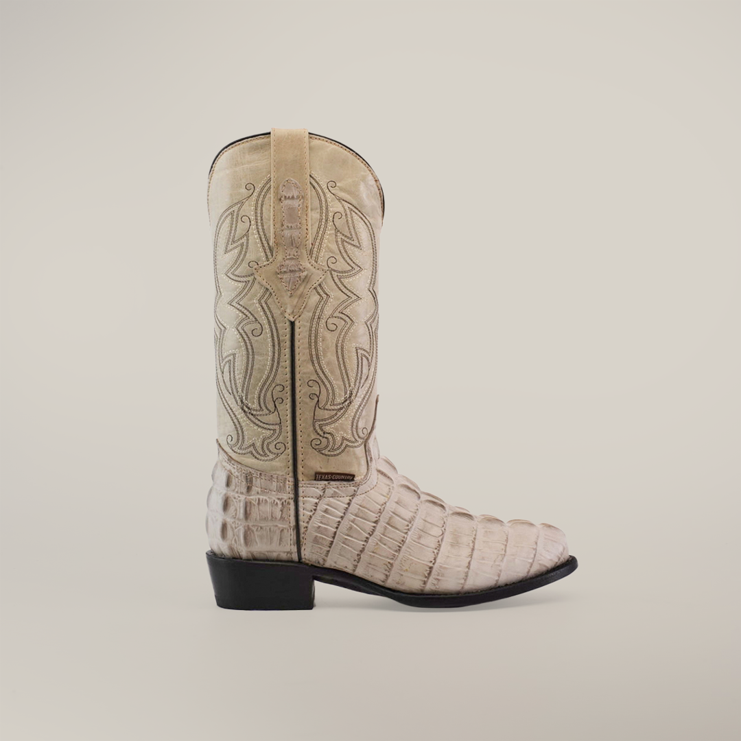 The Crocodile Tail Print Bone - Round Toe is a handmade cowboy boot with intricate embroidery on the upper shaft and a striking crocodile tail print on the lower part. Crafted from premium cowhide in light beige, it features a slightly darker heel and toe, elegantly displayed against a plain white background.