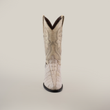 A single white boot, made from premium cowhide, stands upright against a plain backdrop. Featuring intricate patterns on the shaft and a crocodile tail-like textured foot, it has a dark sole and round toe. This is the Crocodile Tail Print Bone - Round Toe boot.