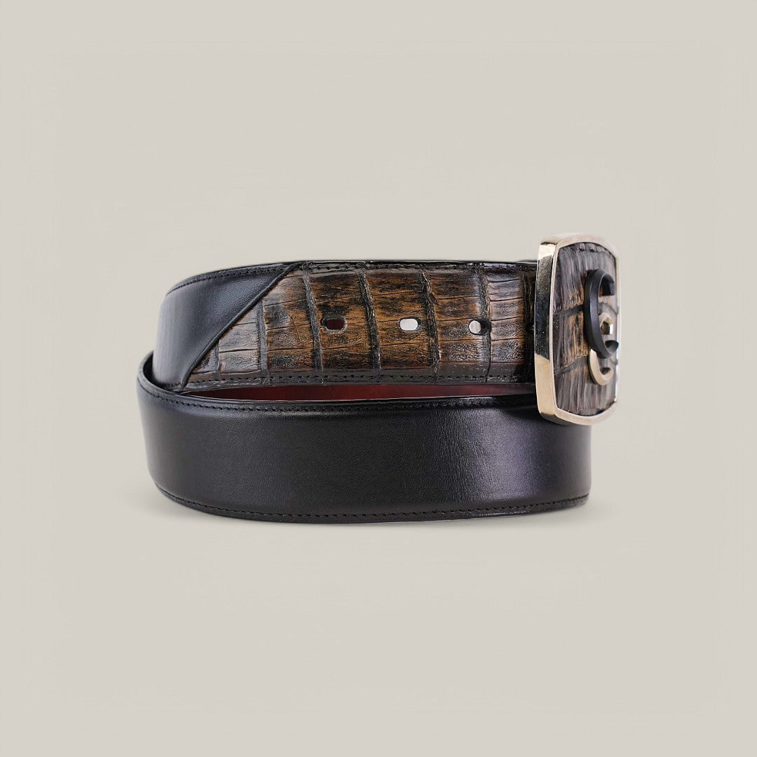 The Black & Brown Caiman Exotic Strip Belt - BC322 is a luxury accessory with a coiled black design featuring caiman leather texture. It comes with a glossy silver buckle adorned with carved details, set against a plain light grey background.