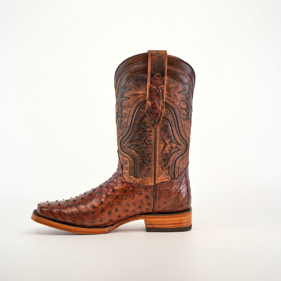 The Exotic Ostrich - Brown - Rodeo Toe is a brown cowboy boot with superior craftsmanship, featuring decorative stitching on the shaft and a rugged ostrich leather surface. It includes a wooden sole and pull strap, elegantly displayed against a plain white background.