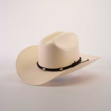 The 1000X Sinaloa Straw Hat is a cream-colored cowboy hat with a wide brim, featuring exceptional quality and a black braided band adorned with small silver embellishments, set against a plain white background to highlight its elegant design.