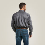 Man with short hair, facing away, wearing the Team Logo Twill Classic Fit Shirt in gray and blue jeans. The shirt has embroidered details and is paired with a brown belt. His hands are in his pockets against a plain light-colored background.