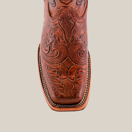 A single handcrafted brown cowboy boot, the Handtooled Leave Cogñac, stands on a white background. Made from premium cowhide leather, it features intricate patterns and stitching with a rodeo toe design that highlights its artisanal craftsmanship.