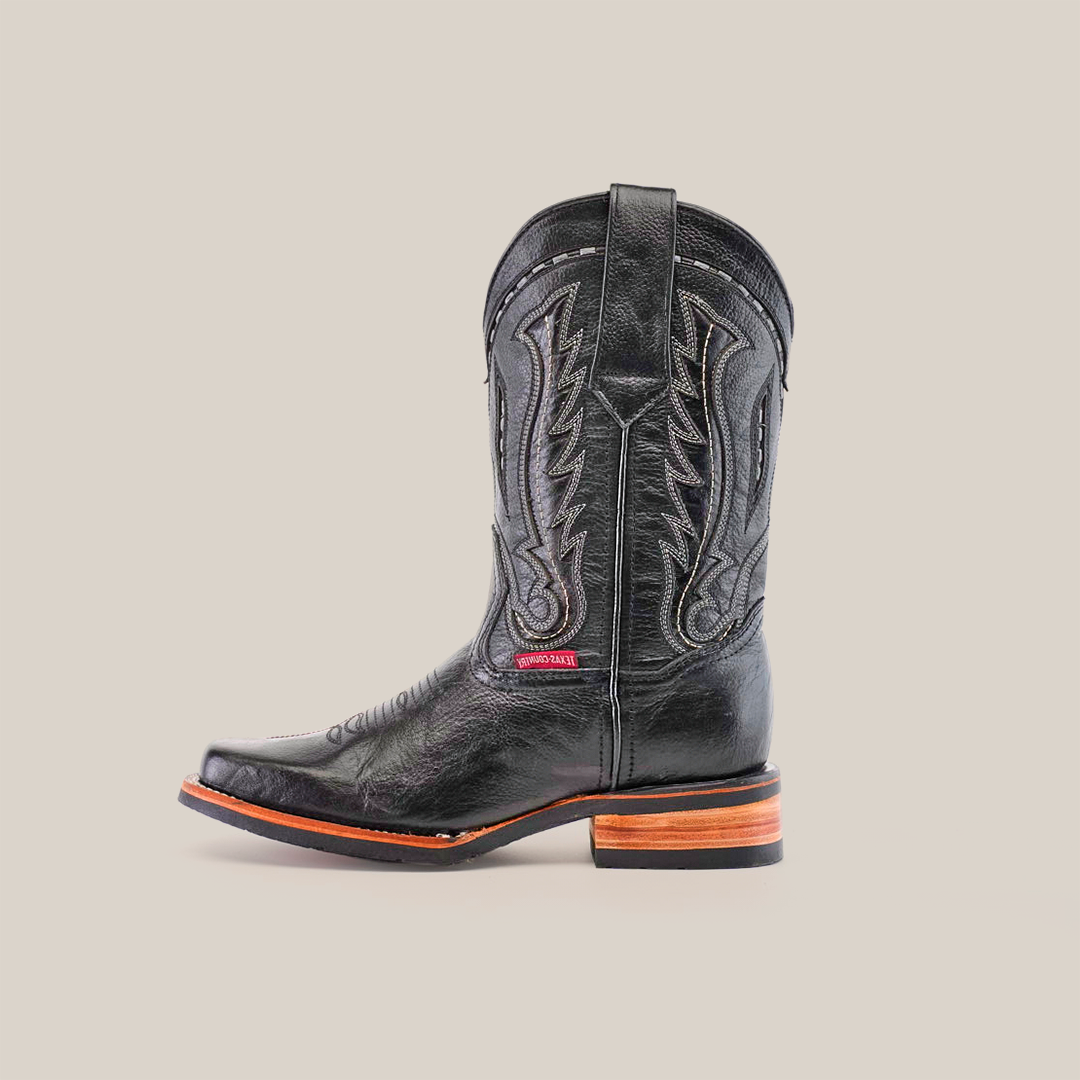 The Barcelona Black boot, made from premium cowhide, showcases decorative stitching and a rodeo toe. It pairs a stacked brown and black heel with a slip-resistant sole. Set against a plain white background, the boot features a subtle side label.