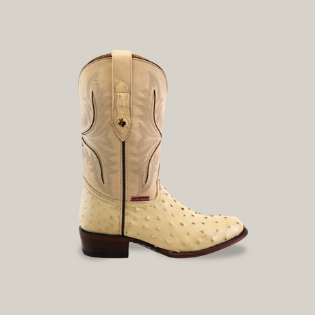 The Exotic Full Quilt Ostrich Boot in Bone is made from genuine ostrich leather, showcasing a stitched shaft pattern. It features a round toe, small bumps, dark heel, pull tab, and is handcrafted by skilled artisans.