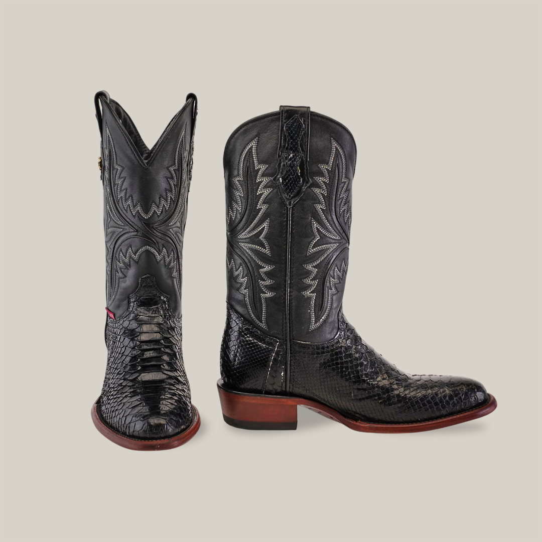 A pair of Exotic Python - Black - Round Toe boots is displayed on a neutral background. These handcrafted cowboy boots feature decorative stitching on the shafts and are made from python leather, showcasing a textured design with dark wooden heels.