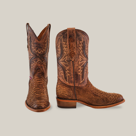 The Exotic Python - Tamarindo boots, featuring a rich brown hue, highlight Western Heritage with intricate stitching and a textured leather pattern. One boot shows its side standing upright, while the other displays the front view, complemented by a wooden heel and rounded toe.