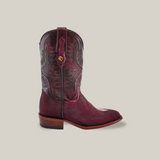 The Exotic Stingray - Wine cowboy boot boasts intricate embossed patterns on its shaft and a distinct emblem on the pull strap. Crafted from luxury stingray leather, it features a textured toe and heel, set against a plain beige backdrop.