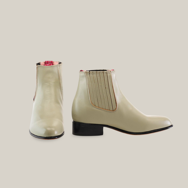 A pair of light beige Napa Bone - Round Toe ankle boots with a small heel and elastic side panels sits against a white background. The left boot faces forward, and the right showcases detailed stitching, highlighting their handcrafted quality. Part of our western wear collection.
